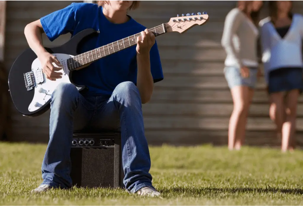 Guitar player sitting on a small tube amp.