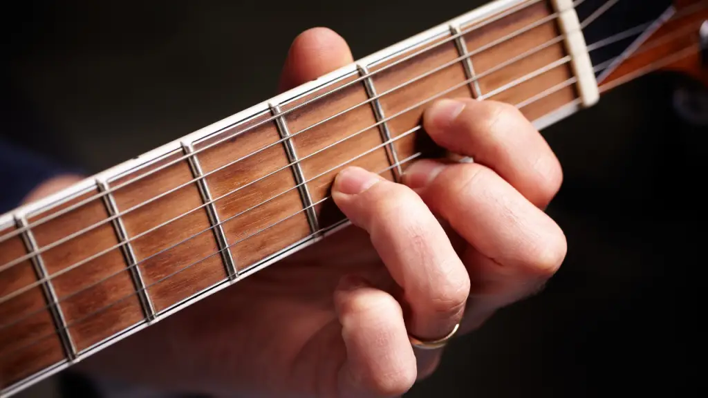 Fingers shaping a D chord on a guitar's neck.