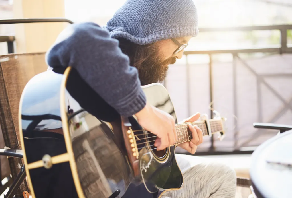 Man in blue hoodie playing black acoustic guitar