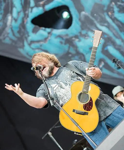 Black singing and playing an acoustic guitar on stage