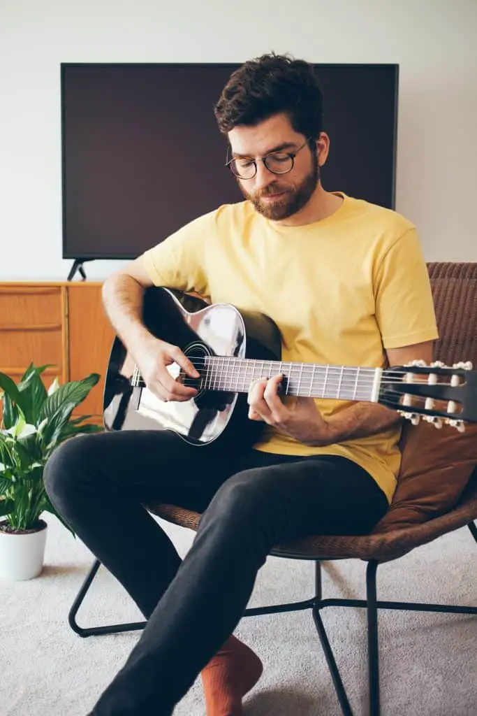 A man sitting in a living room playing guitar