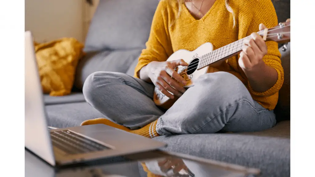 Woman playing ukulele in front of laptop computer